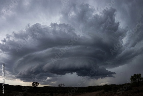 A dramatic swirling storm cloud looms over a barren landscape. Dark gray clouds create a menacing atmosphere, hinting at an impending storm.