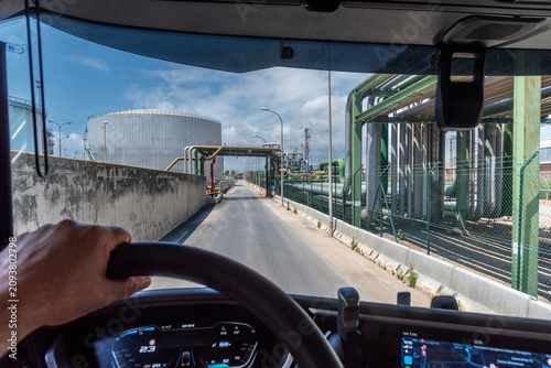 View from inside  commercial truck cab driving through industrial complex with pipelines and storage tanks