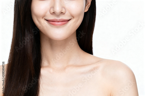 A close-up portrait of a woman with long straight dark hair, smiling softly against a plain white background. The even lighting highlights her smooth skin and natural beauty.