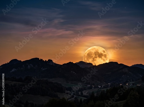 Spectacular full moon illuminating a serene mountain range under a twilight sky, showcasing the majestic beauty of nature at dusk
