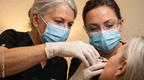 Surgeons performing cosmetic facial injection on senior patient