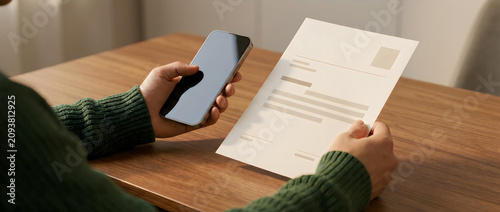 Person holding a smartphone and a document at a wooden table in a professional setting