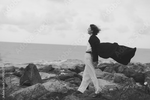 Canvas Print Wind swept coat flows as a woman walks along jagged shore by the sea, capturing