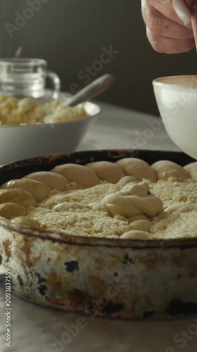 Female hand applying egg wash with a pink brush on a pie crust in a round baking dish, surrounded by bowls of ingredients on a kitchen countertop