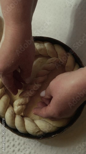 Female baker skillfully weaves braided dough into a circular shape inside a round baking pan on a textured countertop with a clean, bright background
