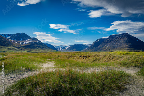 Mountains and grassy fields in Isafjordur Iceland with blue sky and clouds in the background