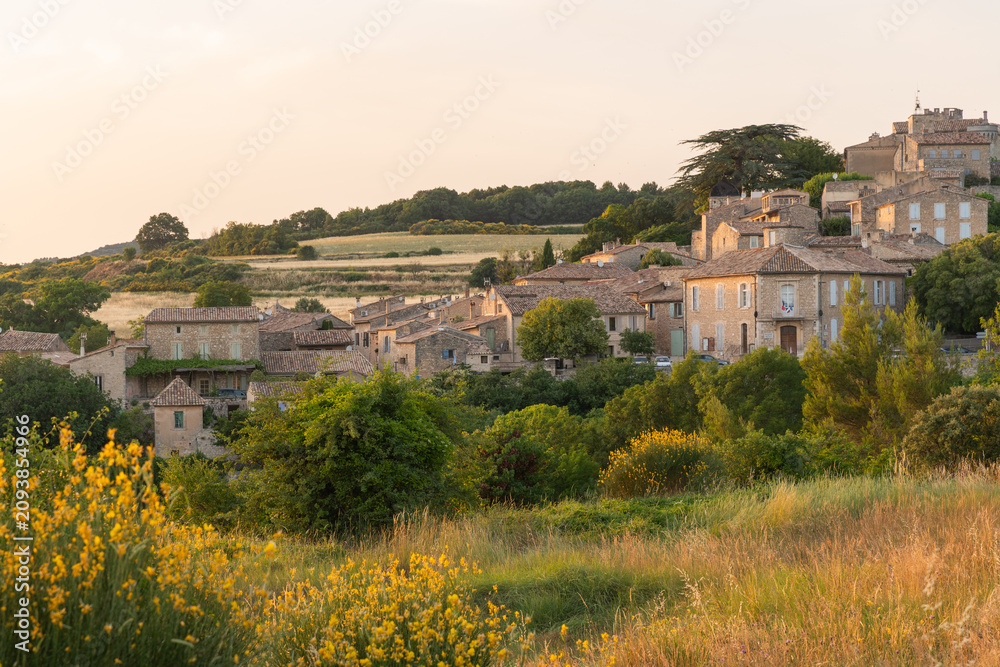 Obraz premium Golden evening light falls across the hillside village of Murs in the Vaucluse department of Provence, France, with wildflowers and dry grass in the foreground and stone houses