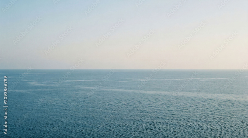 Fototapeta premium The scene shows a vast ocean stretching to the horizon. The sky is light with few clouds. The water is smooth. This is a quiet morning on the coast.