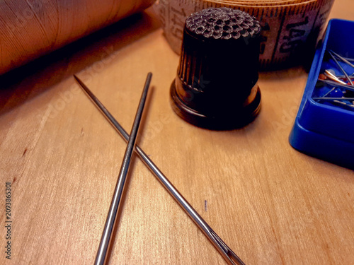 Fotografie Both crossed metal sewing needles rest on a wooden table next to a black thimble