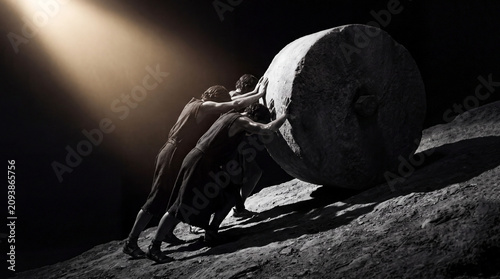 Three figures pushing a heavy stone wheel up a steep incline in a dramatic high contrast spotlight