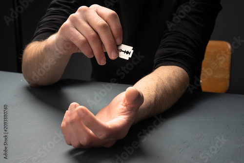 Tableau sur toile Distressed individual holding a razor against the wrist, depicting a suicide attempt and severe emotional crisis, highlighting the importance of mental health awareness, intervention, and support