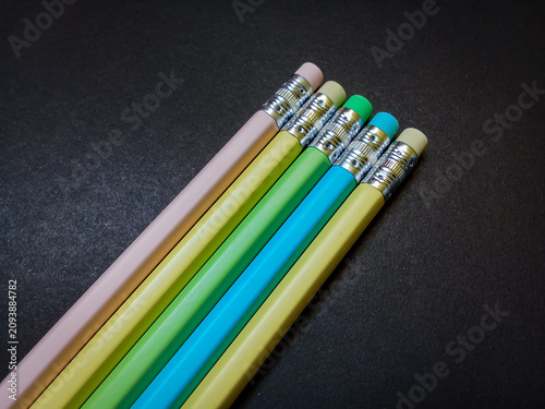 Foto Five unsharpened pastel colored pencils with attached erasers arranged diagonally on a dark textured black background