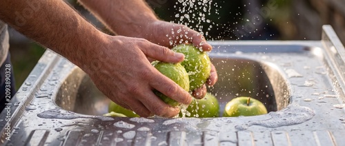 Close up of hands rinsing fresh green apples under flowing water in a stainless steel sink for healthy organic food preparation and daily kitchen hygiene routine
