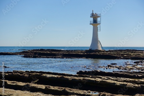 White Aoshima Lighthouse standing on fluted wave-cut rocks with textured foreground
