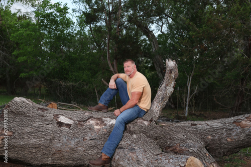 Fényképezés Middle aged man sitting and relaxing on a felled tree in the country surrounded