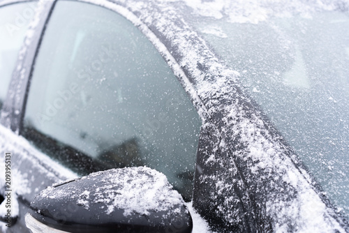Close-up of a dark car partially covered with fresh snow and frost.