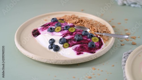 Thick yogurt swirled with vibrant berry compote is served on a textured ceramic plate with fresh berries and cereal. The soft natural side light highlights the creamy consistency and rustic details.