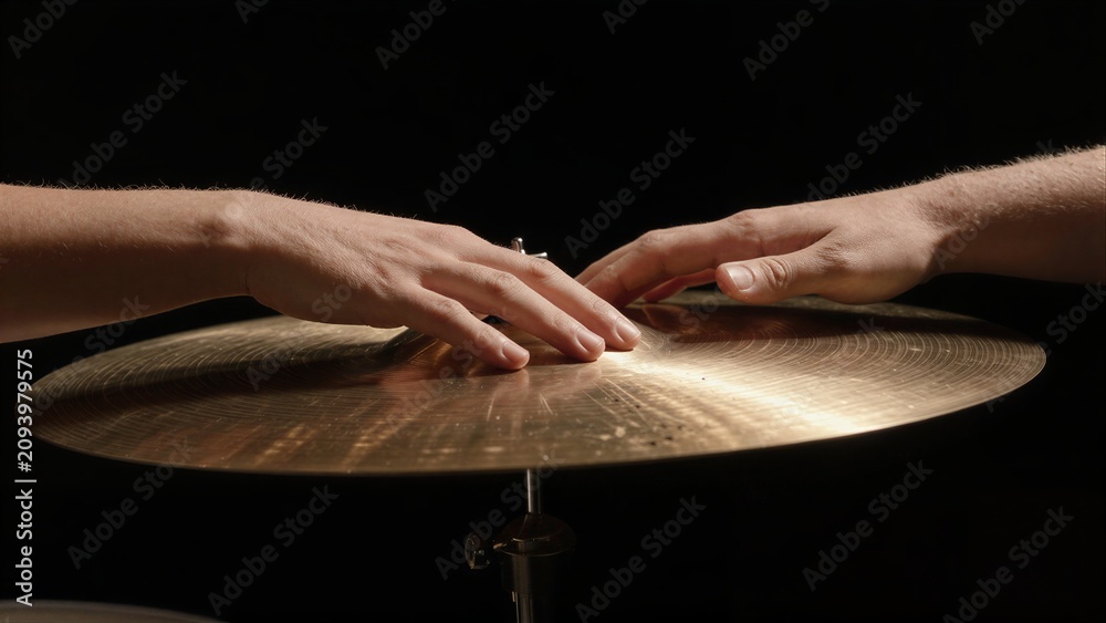 Obraz premium Two hands gently touch golden cymbals against a dark background.