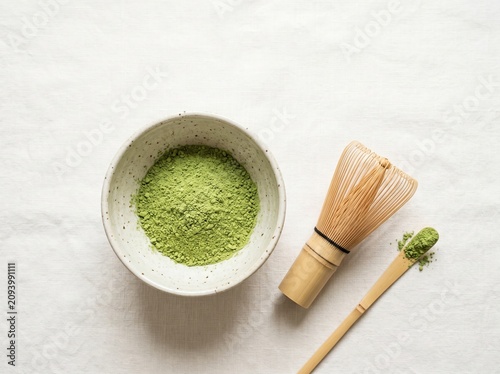 Принти на полотні Overhead shot of vibrant green matcha tea powder in a ceramic bowl, accompanied by a traditional bamboo whisk, on a clean white surface, highlighting healthy beverage preparation