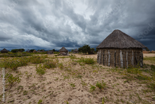 фотографія Rain filled dark storm clouds overtake Okavanga village with its round straw hou