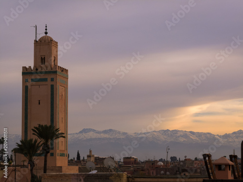 Картината върху платно The suns rays shine briefly on the snow capped mountains behind Marrakesh minare