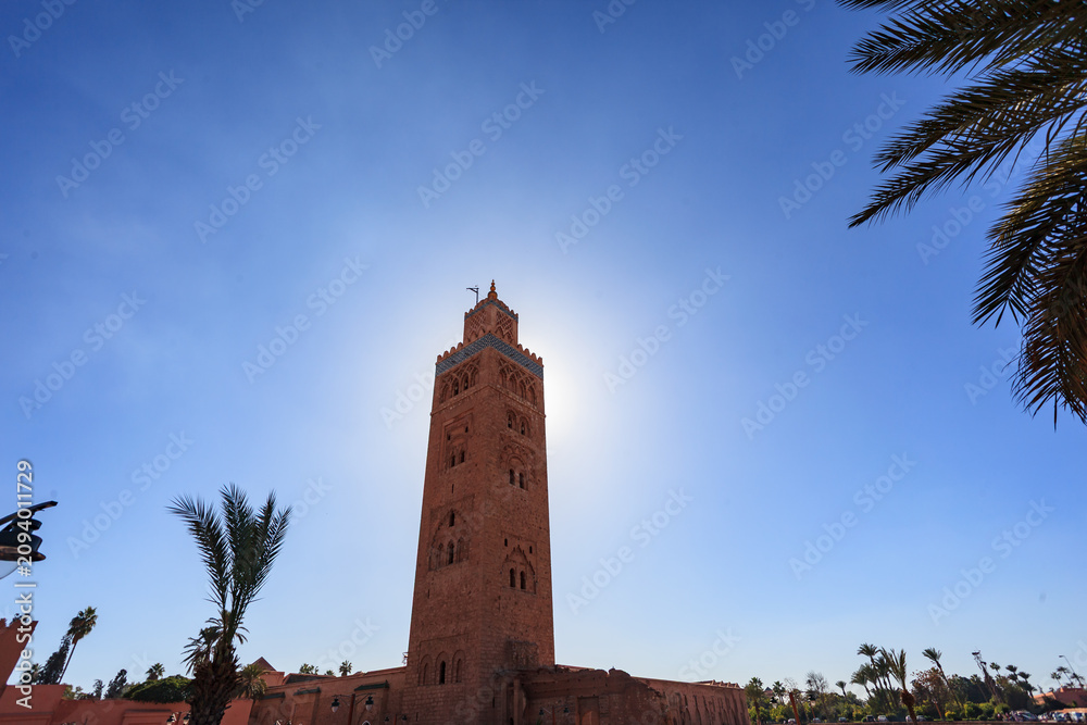 Fototapeta premium A low-angle shot of the Koutoubia Mosque in Marrakesh, Morocco, showcasing its minaret against a clear blue sky, highlighting its architectural details and cultural significance.