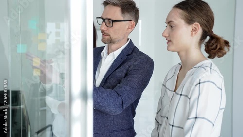 Business team collaborating on a project, analyzing data on a tablet, planning strategy with sticky notes on a glass whiteboard in a modern office meeting