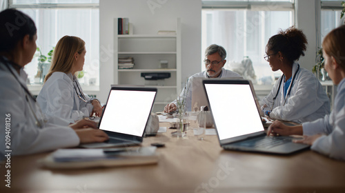Modern healthcare startup office where doctors and software developers collaborate around a table discussing digital healthcare innovation, generic laptops with blank screens