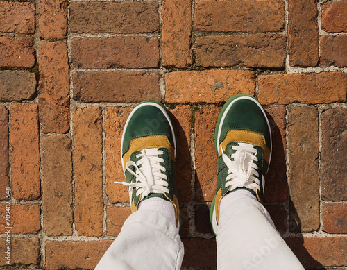 Photograph of green and yellow sneakers on brick walkway from top-down perspective outdoors