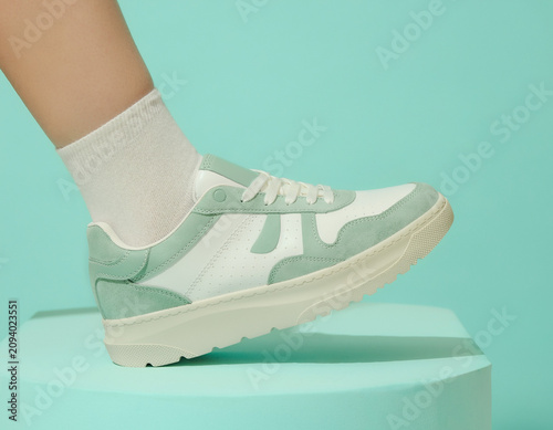 Close-up View of Foot on Mint Green Platform Wearing Sneaker in Studio Setting with Soft Lighting and Casual Atmosphere