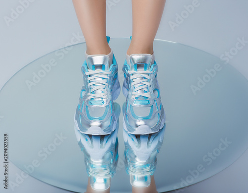 Close-up view of shiny silver sneakers with blue accents on reflective surface, showcasing modern style and calmness
