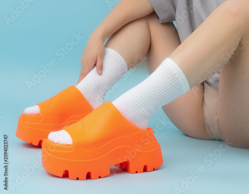 Close-up View of Person's Feet in Vibrant Orange Shoes with White Accents on Bent Knees in Gradient Environment