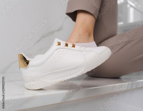 Sitting Person Showcases Athletic Shoe on Marble Step with Gold Accents in Minimalist Environment from Direct Viewpoint