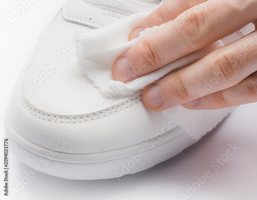 Close-up view of hand cleaning a white sneaker with cloth on a plain surface from top-right perspective in instructional context