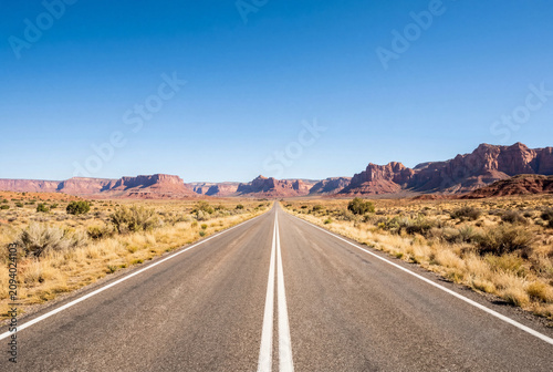 Long straight highway through a vast desert landscape with red rock mountains