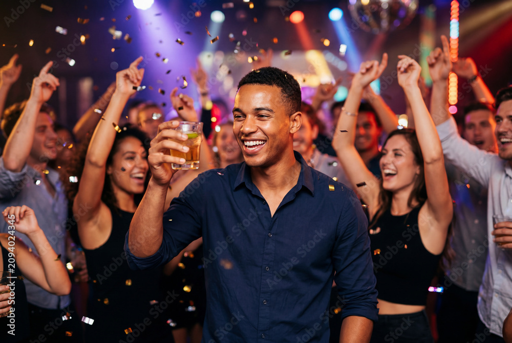 Obraz premium Group of joyful friends celebrating with drinks and confetti in a nightclub