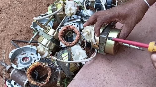 Unscrewing Bolts on Discarded Fan Motor Using Hand Screwdriver. Electric Motor Manual Dismantling and E-Waste Recycling Process in Workshop