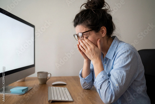 Weary woman rubbing her tired eyes while working at a computer desk