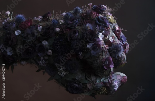 clenched fist shape constructed entirely of densely packed flowers dark moody roses anemone thistle deep jewel tones dramatic side light dark background