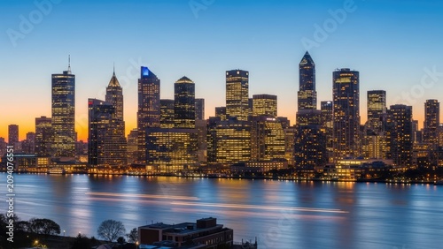 Illuminated city skyline reflecting in water at twilight hour.