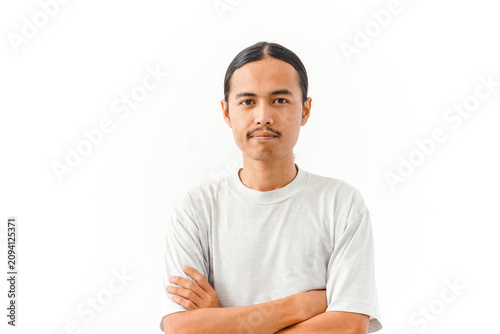 A young man with long dark hair tied back and a mustache stands with his arms crossed against a white background.