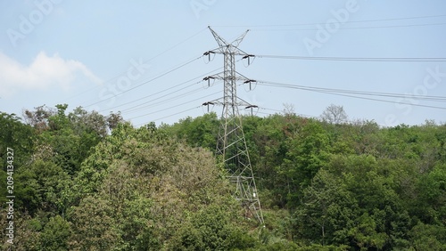 Industrial power line infrastructure distributing energy through metal lattice tower structures surrounded by rural jungle trees.