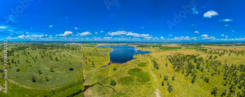 A panoramic shot of a big green field at Rangers Vally Cattle with beautiful blue sky in Australia with a swamp in the middle
