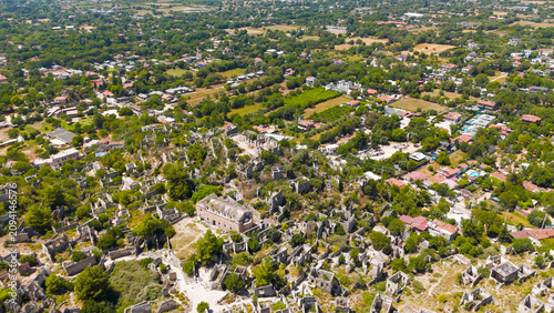 Kayakoy, Turkey. Aerial drone view of the Upper Church (Panagia Pyrgiotissa) among abandoned ghost town ruins on mountain slope under clear sky.. Aerial View