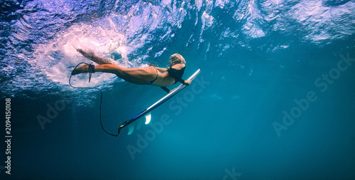 Underwater shot of female surfer diving with surfboard in clear