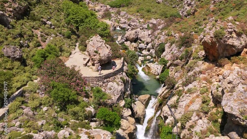 Aerial drone view of a rocky river with small cascades and turquoise pools between boulders and pink oleander, Kourtaliotiko Gorge, Greece