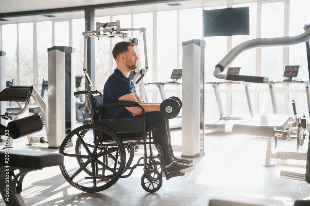 Obraz premium Man in wheelchair lifting dumbbells during rehabilitation in gym