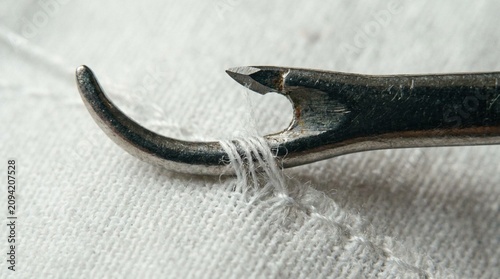 Close-up of a metal sewing awl stitching white thread through fabric with a shallow depth of field on a clean background.