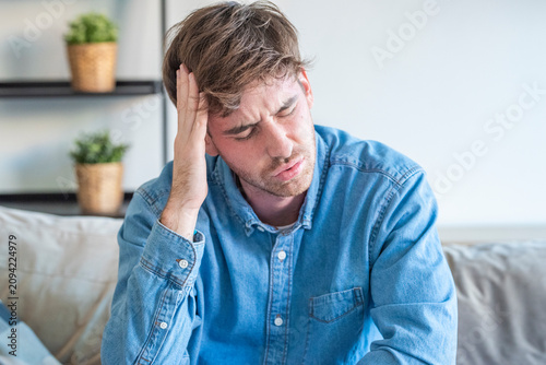 Cuadro en lienzo Young man suffering from headache and stress at home, holding his head in pain o