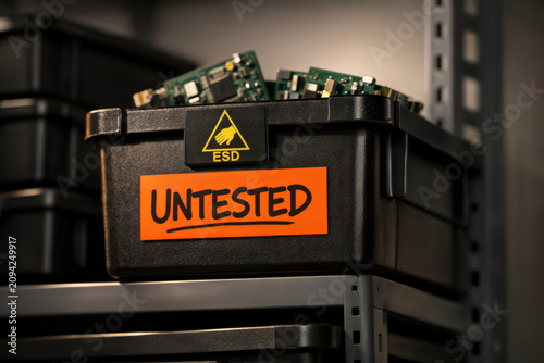 Untested electronic circuit boards in an ESD bin on a warehouse shelf.